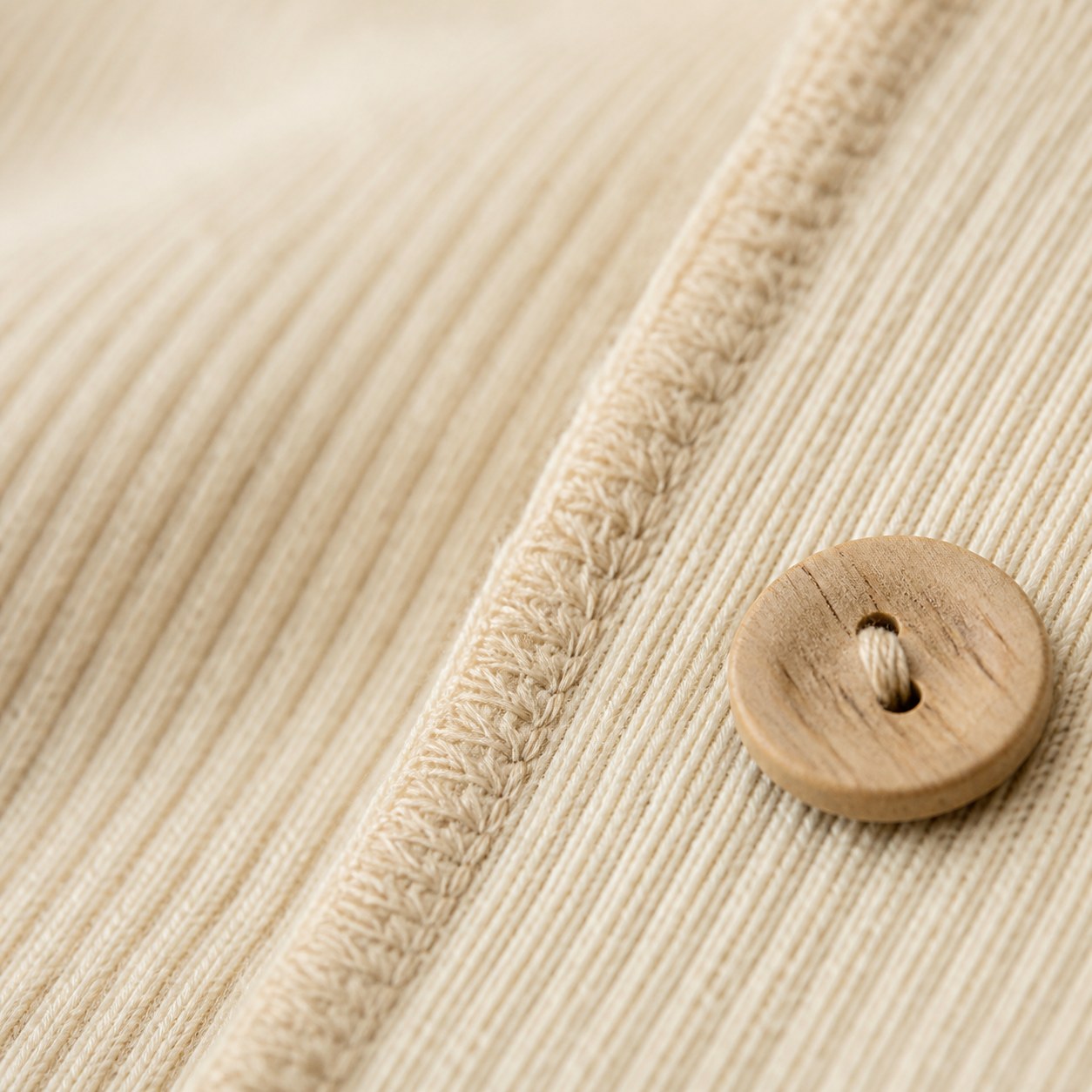 Macro detail of cream rib knit, a flatlock seam and wooden button
